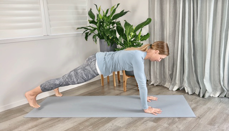 woman practicing plank pose on yoga mat with wide legs.
