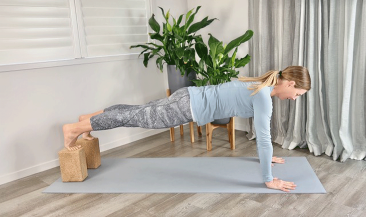 Woman practices plank pose with feet on blocks
