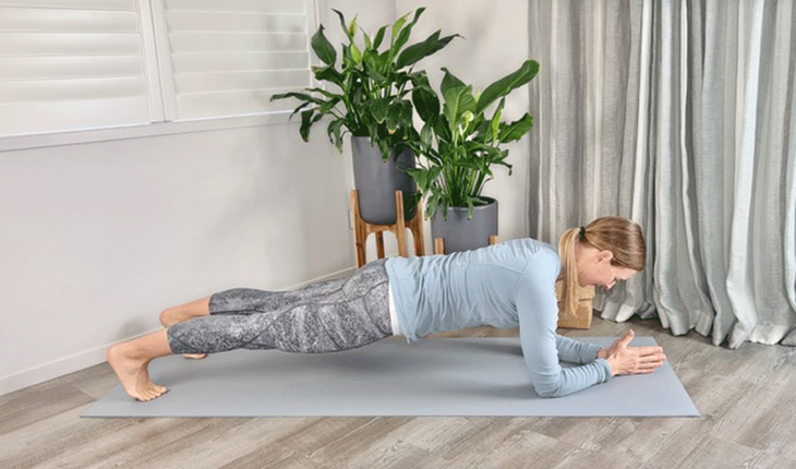 A woman practices a forearm plank on a yoga mat