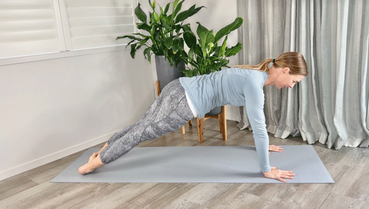 Woman practicing Plank Pose on a yoga mat with her heels leaning to one side