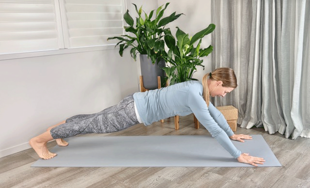 Woman practicing Plank Pose with hands in front of her shoulders on the yoga mat