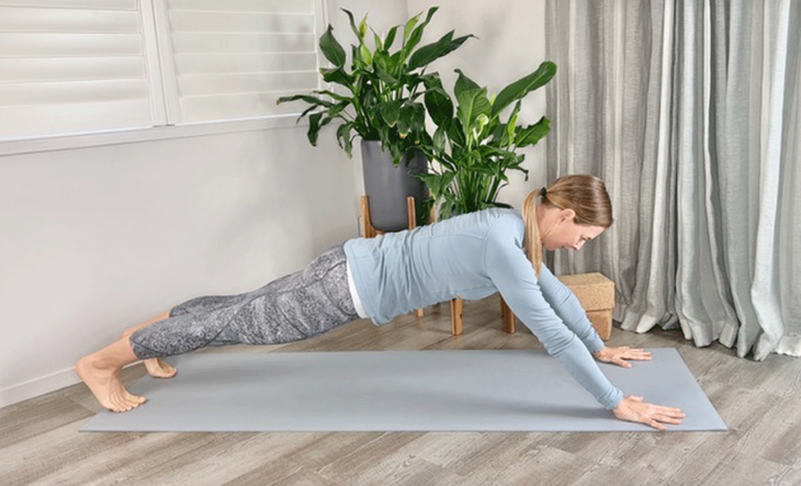 Woman practicing Plank Pose with hands in front of her shoulders on the yoga mat