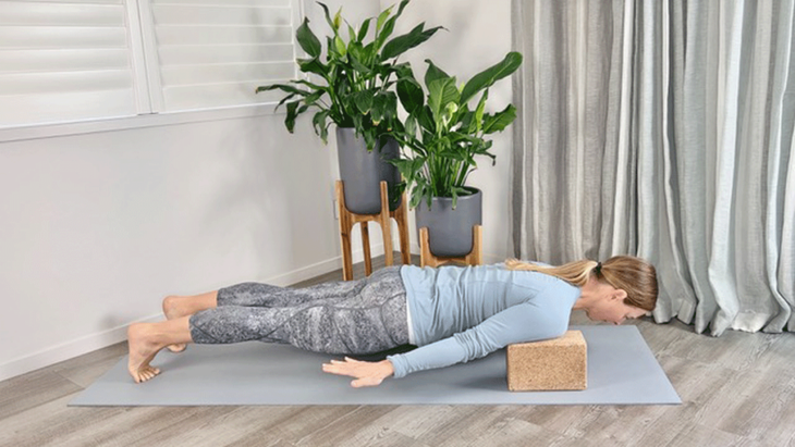 A woman practices plank pose on a yoga mat with blocks under her shoulders