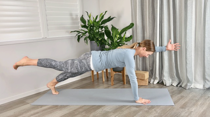 Woman in plank pose on yoga mat with opposite leg and arm extended straight