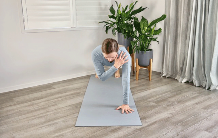 A woman practices plank pose with one hand touching the opposite shoulder