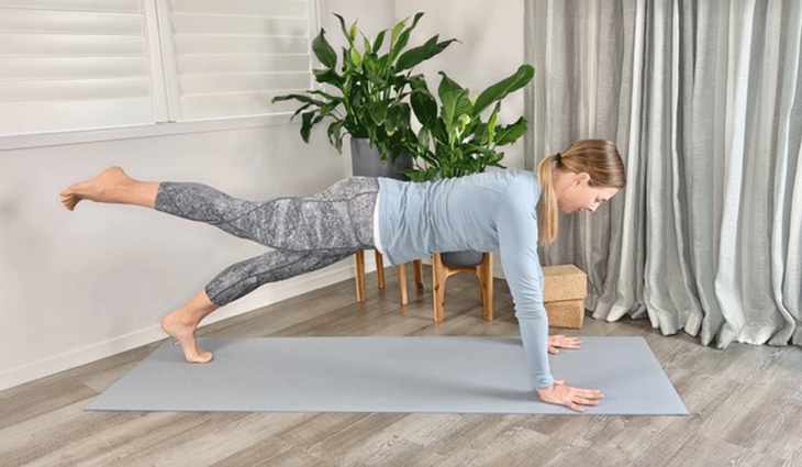 Woman practicing Plank Pose with one leg lifted off the yoga mat