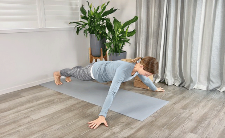 A woman practices plank pose, hands wider than shoulders