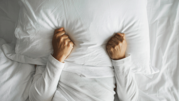 A woman lies in bed with a pillow on her face because she cannot sleep