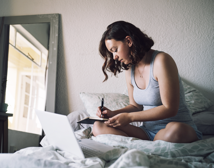 Woman sitting on bed writing in her journal to process her anxiety