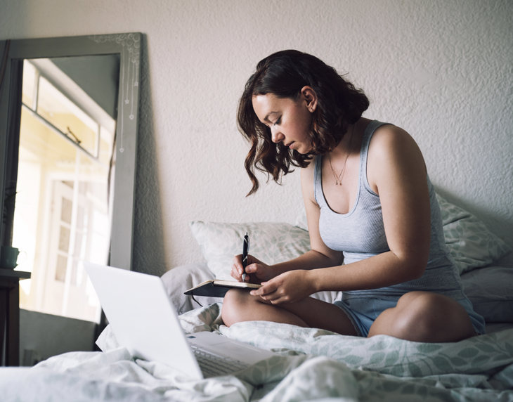 A woman sits on her bed and writes in her diary to relieve her anxiety