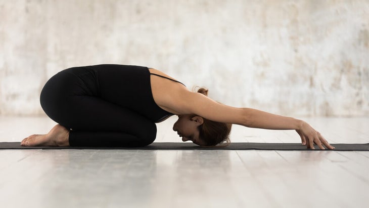 Woman kneeling in Child's Pose or Balasana on her yoga mat to stretch her lower back