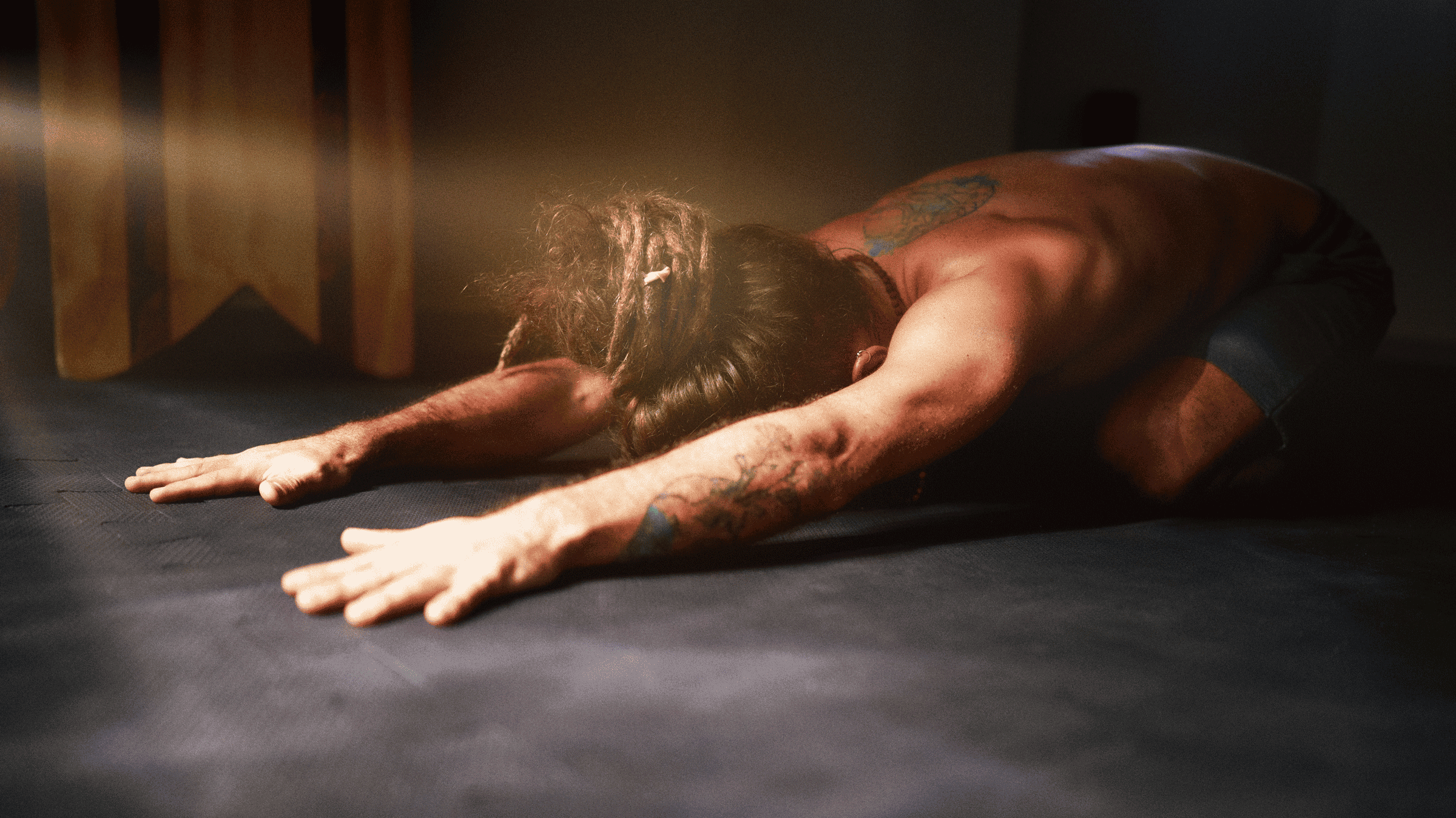 Man with tattoos on his yoga mat practicing Child's Pose