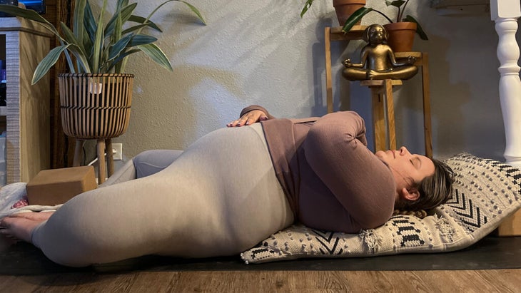 Woman lying on her back on a yoga mat with her knees bent and her feet together while practicing yin yoga