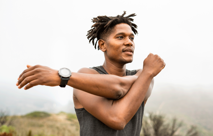 Runner outside on an overcast day practicing a shoulder stretch for athletes