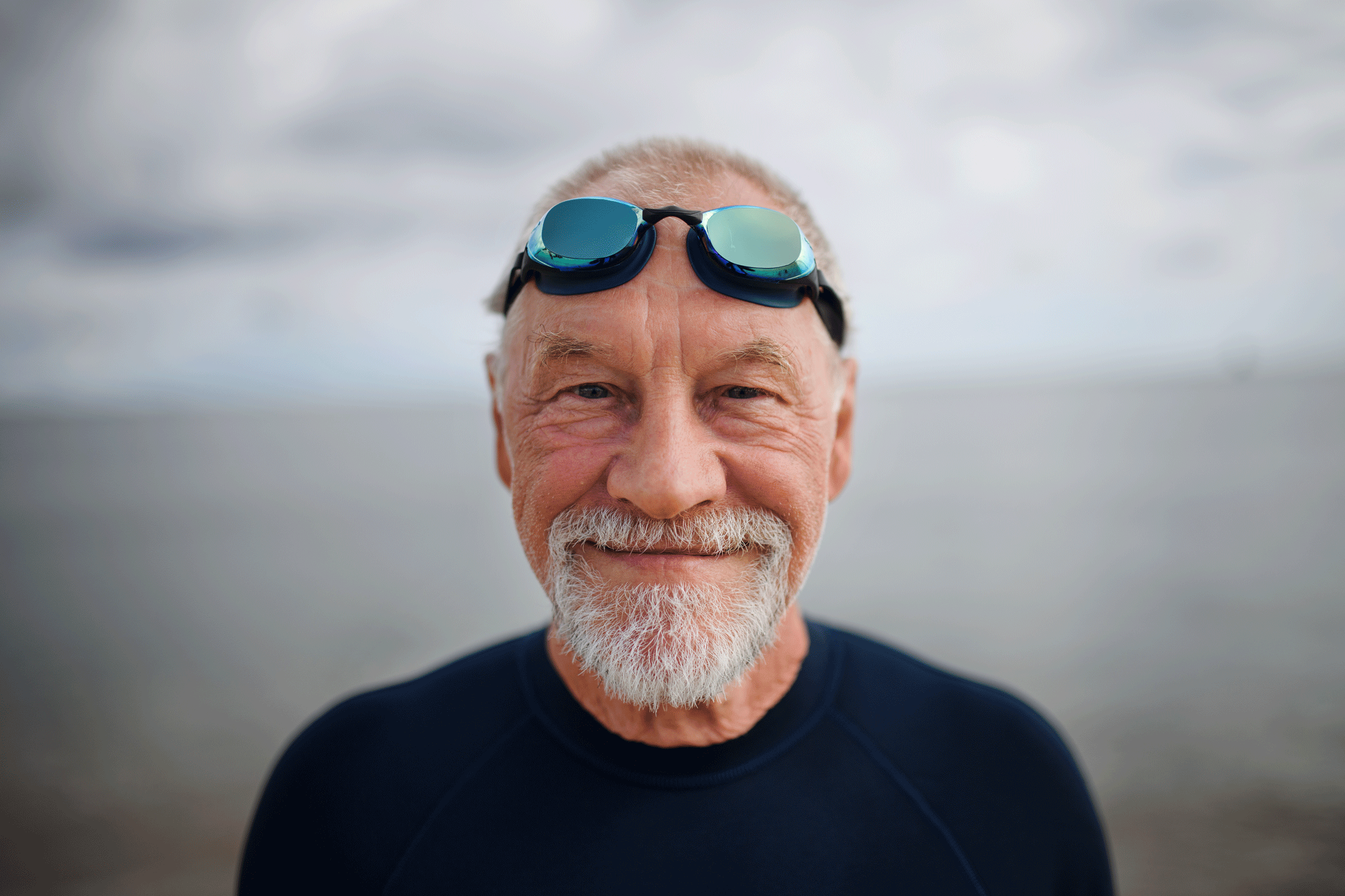 A senior man wearing a wetsuit and goggles grinning at the camera as he returns from a swim in the ocean
