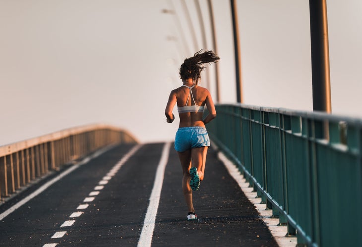 Un corredor corriendo por un puente con pantalones cortos ajustados y un sujetador deportivo.