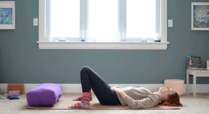 Yoga with Kassandra lying on her back on a yoga mat with her knees resting against each other