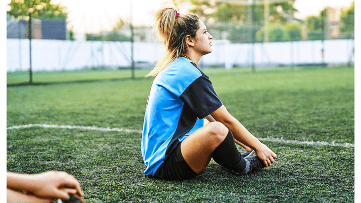 Soccer player sitting on the field practicing Butterfly Stretch