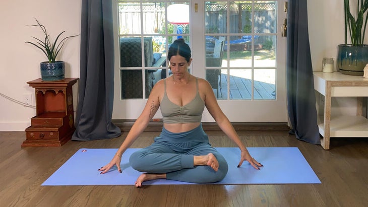 Woman sitting on a yoga mat with her legs crossed in one of many Pigeon Pose variations