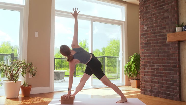 Yoga with Kassandra practicing Revolved Triangle Pose with her bottom hand on the block.