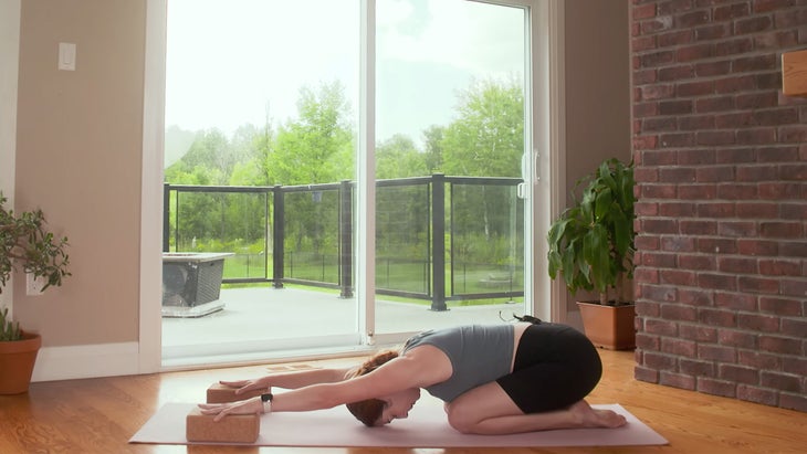 Woman kneeling in Child's Pose with her hands on blocks during a 20-minute power yoga practice