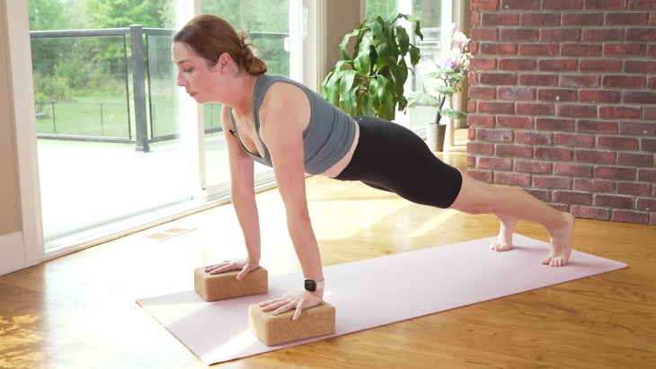 Yoga With Kassandra on a mat practicing Plank Pose with her hands on blocks