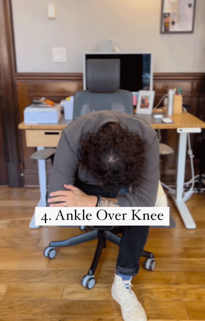Man sitting in a chair with his right ankle crossed over his left knee in a figure-4 shape while practicing desk yoga