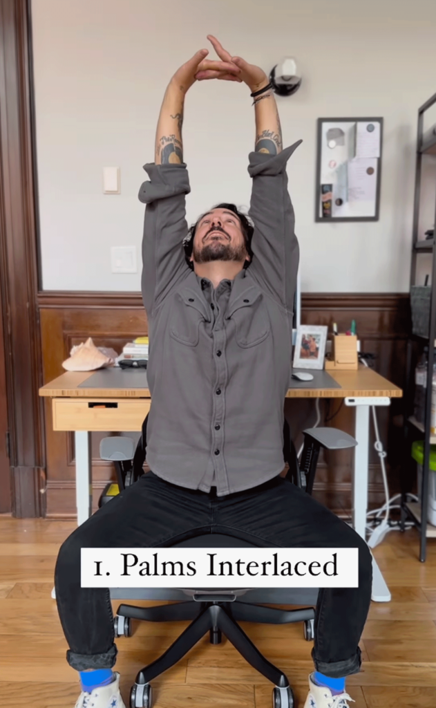 Man sitting at a desk with his fingers interlaced and palms reaching toward the ceiling while practicing desk yoga.