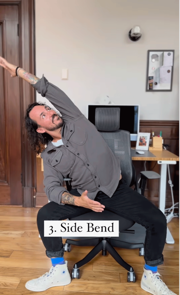 Man sitting in a chair leaning off to one side while practicing desk yoga.