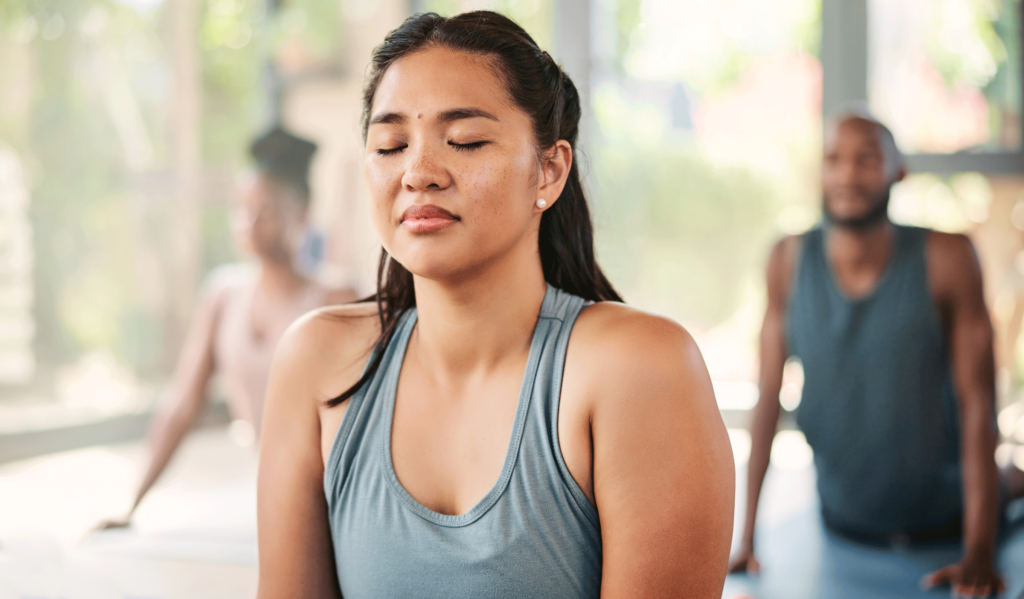 Woman practicing yoga in class with her eyes closed and a smile on her face as she feels supported in practicing what's right in her body