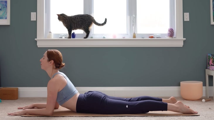 Yoga With Kassandra practices Sphinx Pose on her mat with her forearms on the mat and her chest lifted as part of a 15-minute yoga for stress relief class.