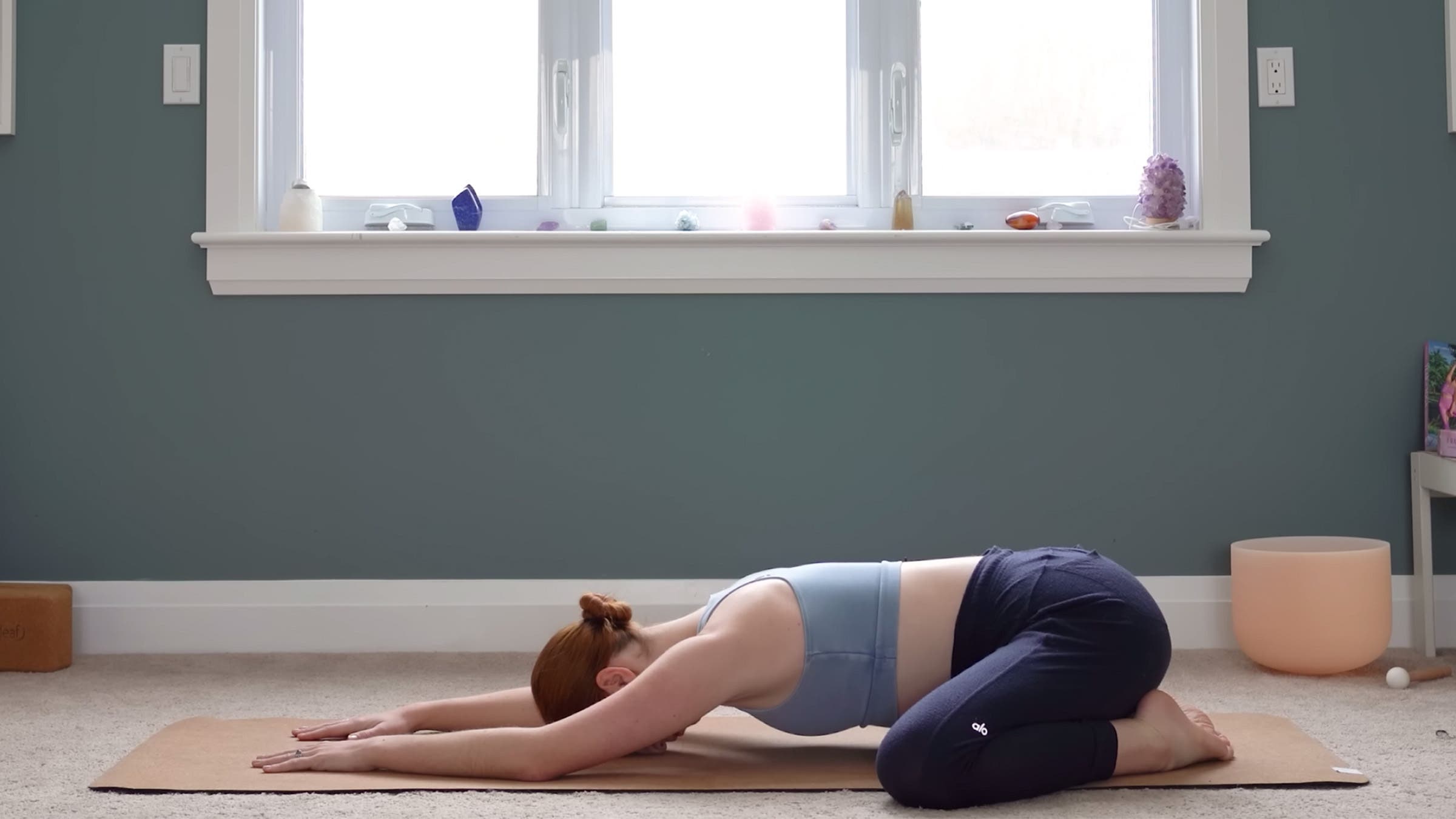 Yoga With Kassandra practices Child's Pose on her mat with her arms extended in front of her during a 15-minute yoga for stress relief class.