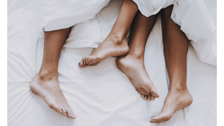 A couple's legs hidden beneath white sheets to demonstrate how the release of oxytocin can bring relief from holiday anxiety.