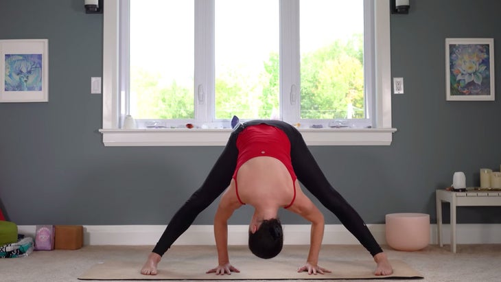 Woman practicing wide-legged forward fold on a yoga mat