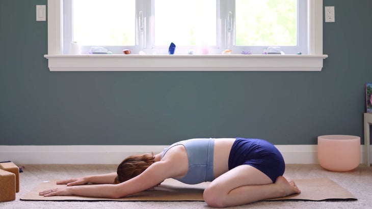 female yoga instructor in child's pose on a mat.