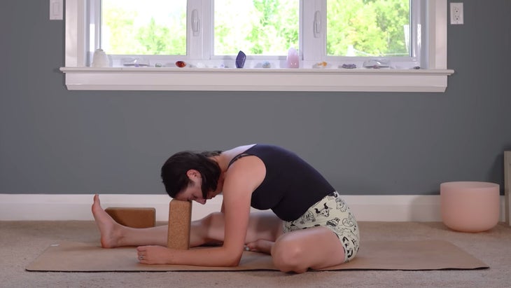 Woman lying on a mat in a stretch with a block beneath her forehead