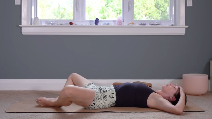 Woman lying on her back with her knees bent and her feet together in a yin stretch for the hips and lower back
