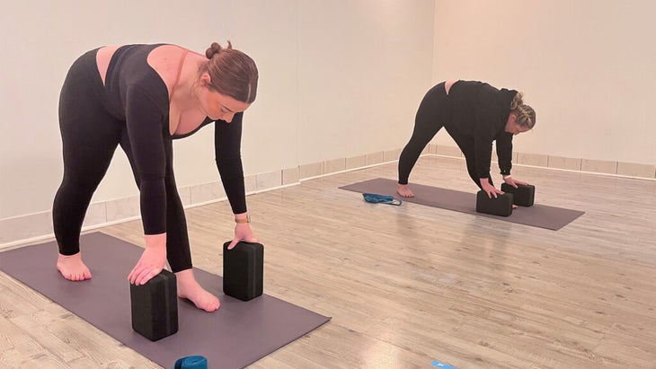 Students on mats practicing Pyramid Pose with blocks beneath their hands to minimize strain along the back body.