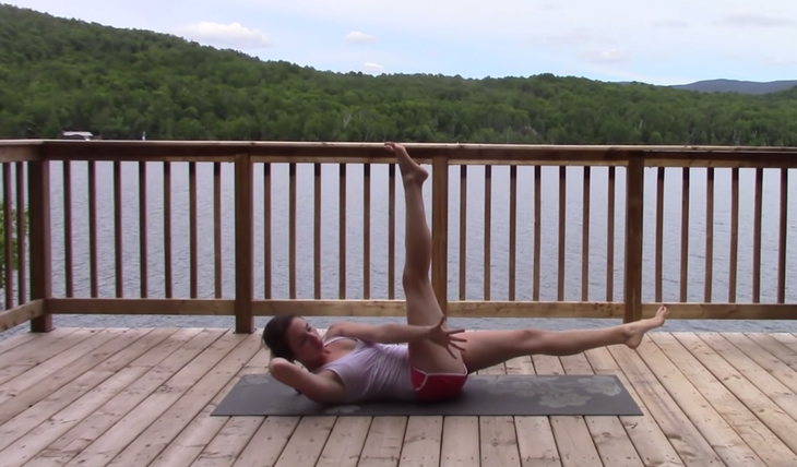 Yoga With Kassandra practicing crunches with an added side stretch while doing a 20-minute yoga practice outside