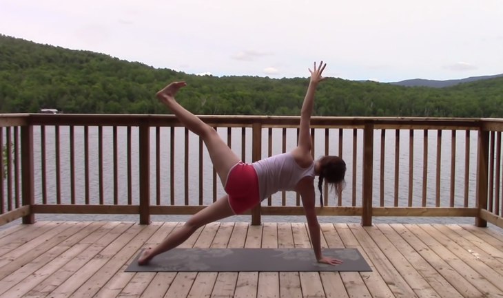 Yoga With Kassandra seated cross-legged outside on a mat practicing Side Plank during a 20 minute yoga class