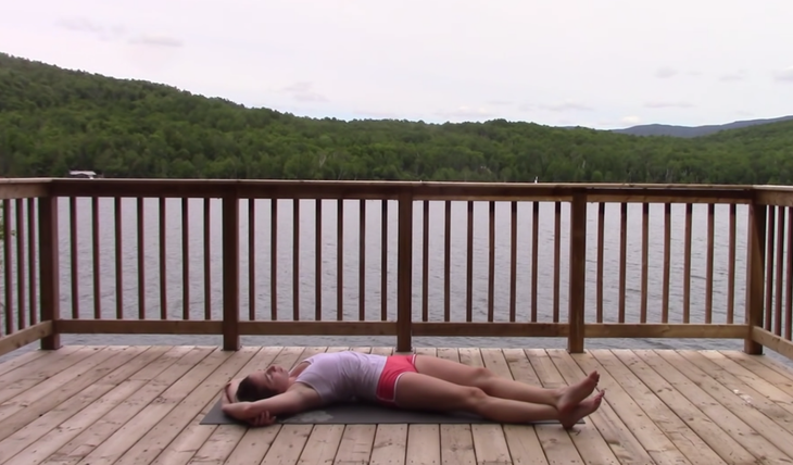 Yoga With Kassandra lies on a yoga mat in a side stretch known as Crescent Moon or Banana