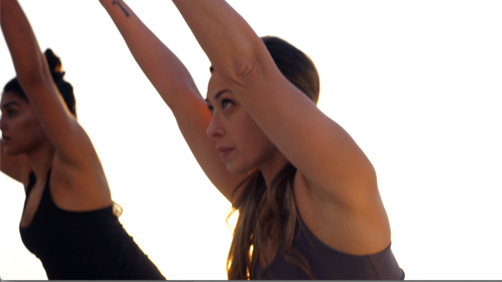 Two women taking an outdoor rooftop yoga class in Chair Pose with their knees bent and their arms alongside their ears