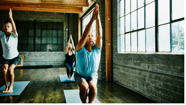 Man working out in Chair Pose during a yoga class contemplating common workout mistakes over 50.