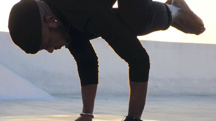 Man practicing Crow Pose by balancing on his hands and lifting his knees to his upper arms