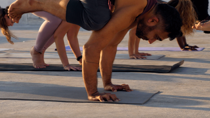 Class of yoga students practicing Crow Pose while using their fingers as brakes and lifting their palms off the mat