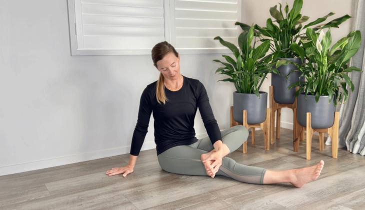 Woman sitting on the floor sliding her fingers in between her toes to stretch