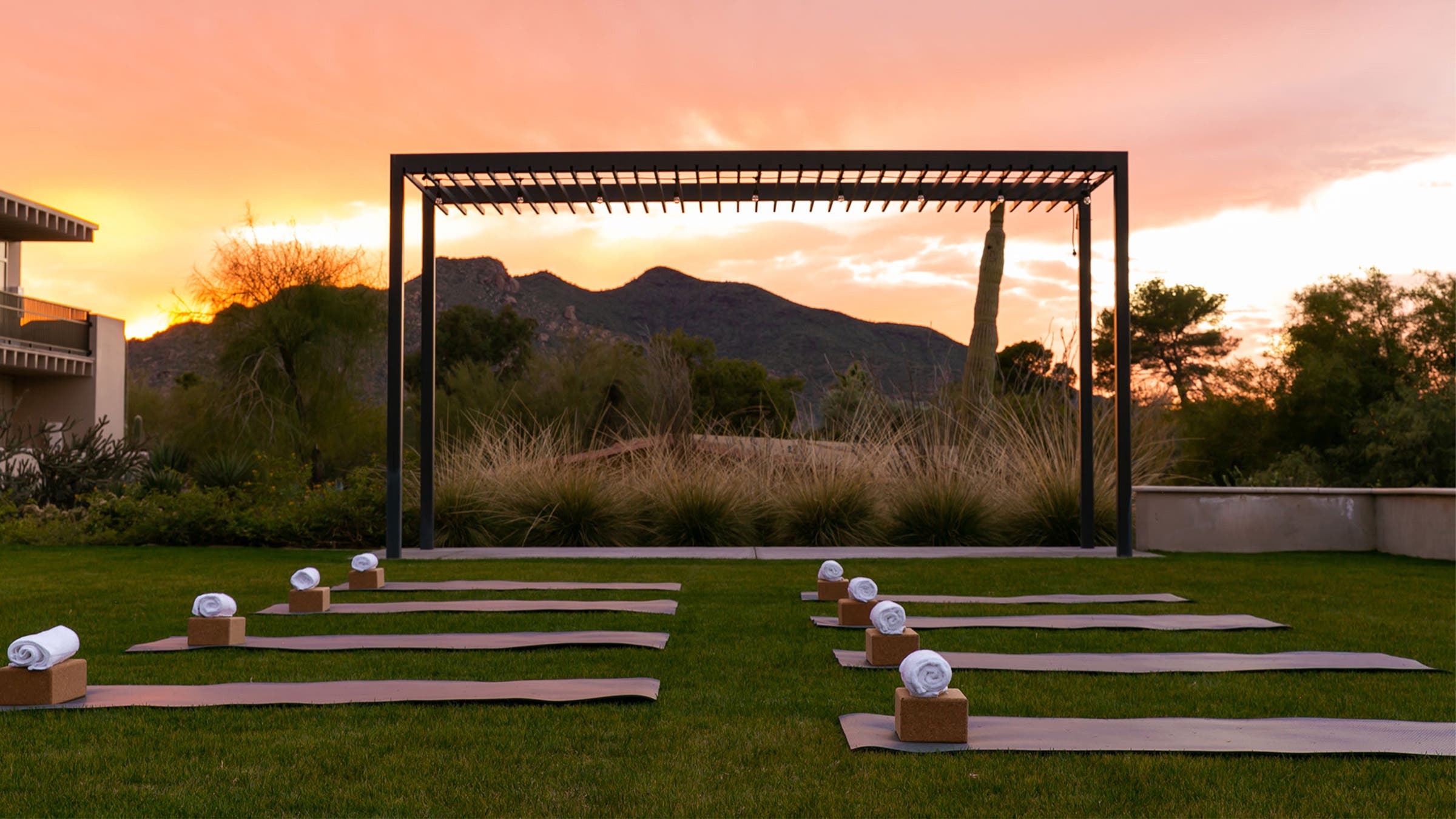 yoga mats set up on a lawn in preparation for a class, with a sunset and mountains in the background at a wellness retreat
