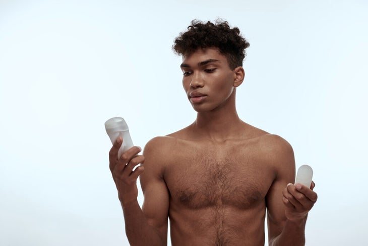 Man holding a stick of deodorant and reading the ingredient list while contemplating why does sweat stink?