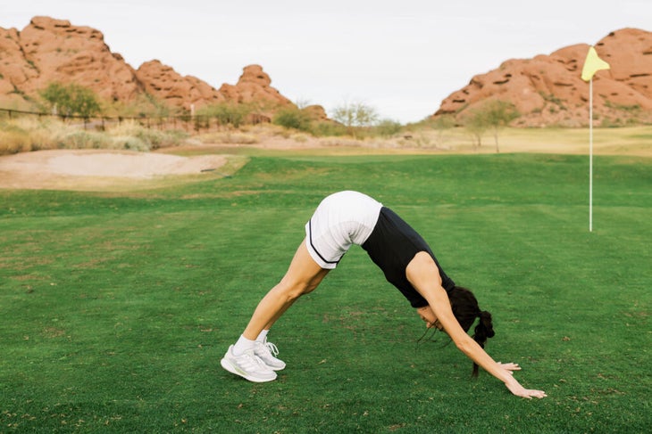 A woman on a golf course with the McDowell red rocks and mountains in the background practicing Downward-Facing Dog as one of several exercises for golfers.