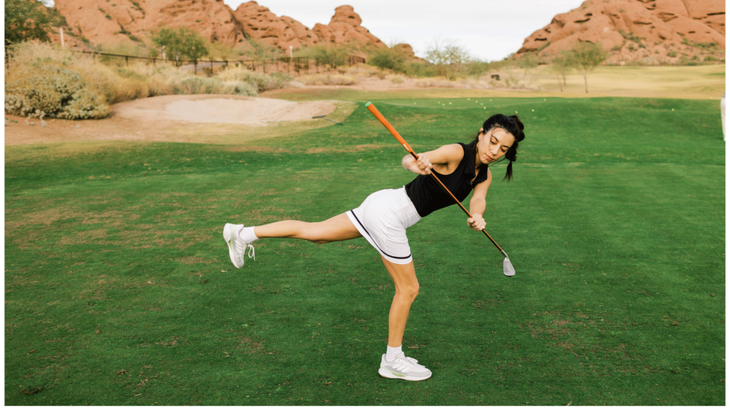 Woman practicing Warrior 3 while holding a golf club on a golf course.